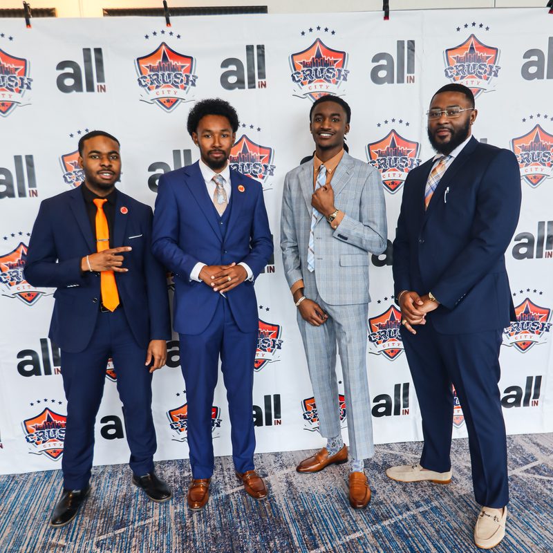 Four Onias Marketing representatives in navy suits at a brand event backdrop